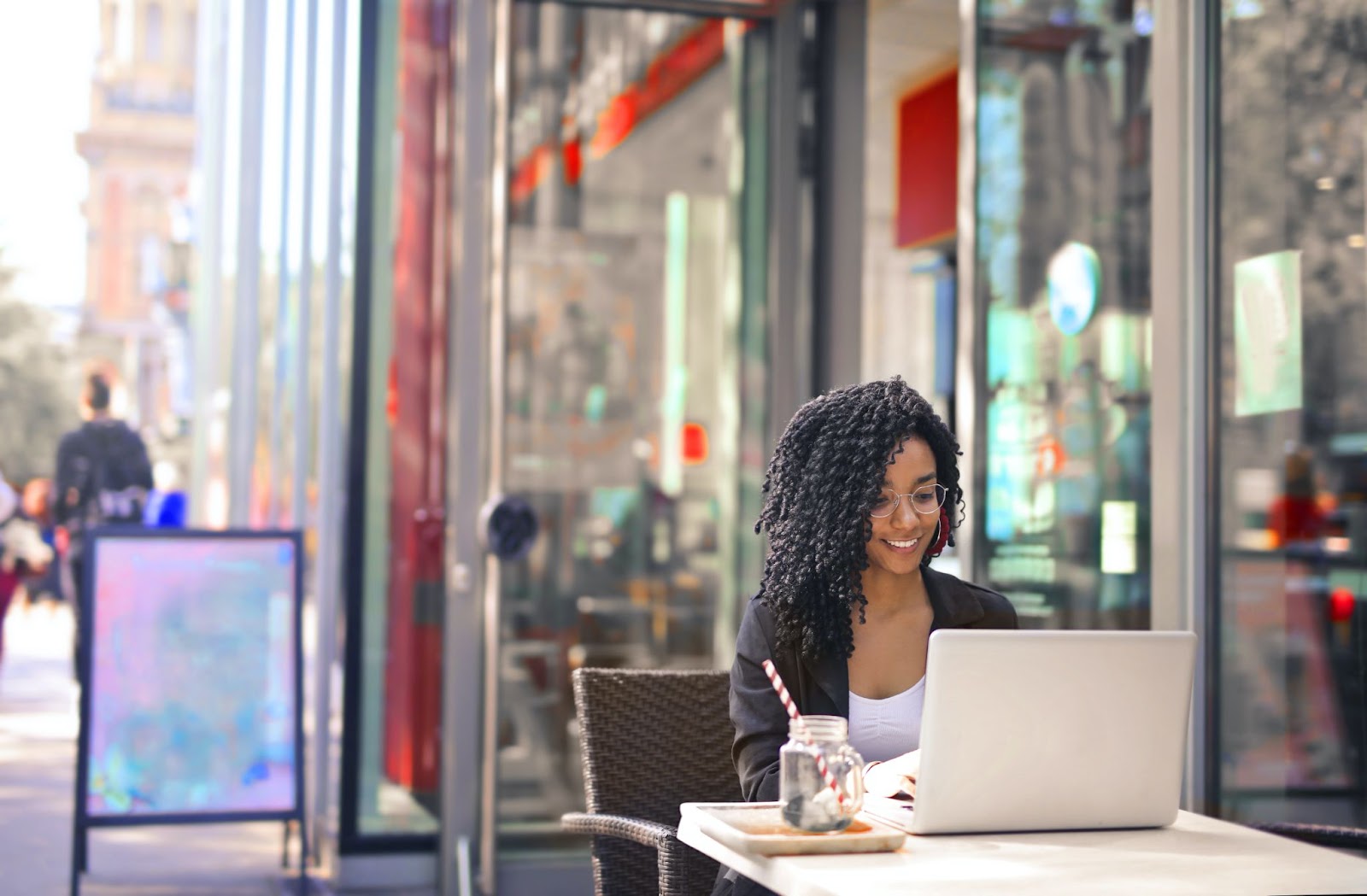 A woman sitting at a table outside a cafe working on her laptop computer as a digital nomad.